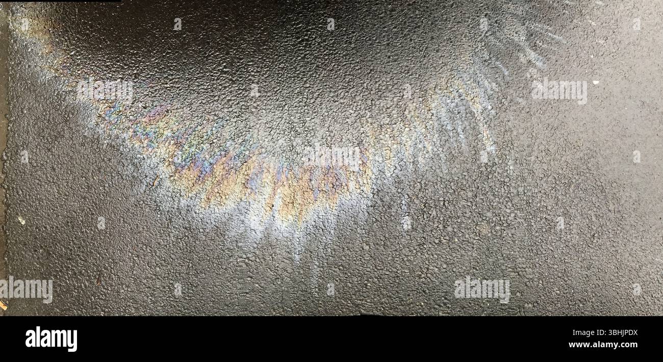 Farbenfrohe Regenbogenmuster entstanden durch Öl auf einer strukturierten, nassen Straßenoberfläche. Das abstrakte Erscheinungsbild zeigt eine Mischung aus lebendigem h Stockfoto