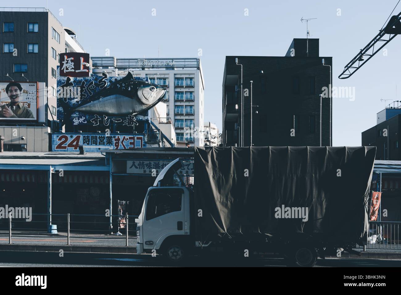 Über einem rund um die Uhr geöffneten Sushi-Restaurant erhebt sich eine riesige Thunfischskulptur, die teilweise von einem vorbeifahrenden Lieferwagen verdeckt wird Stockfoto