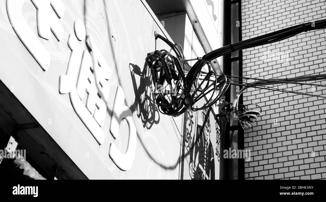 Ein dichter Knoten von elektrischen Kabeln wirft scharfe Schatten auf eine Ladenfront in Tokio Stockfoto
