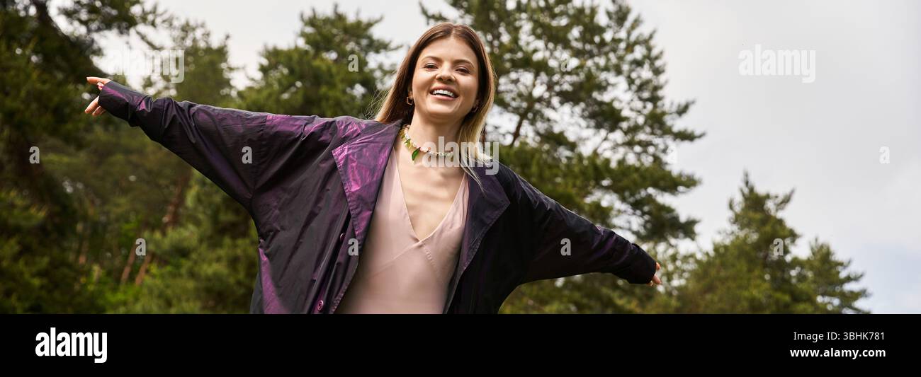 Lächelnde Frau mit offenen Armen im grünen Wald. Stockfoto