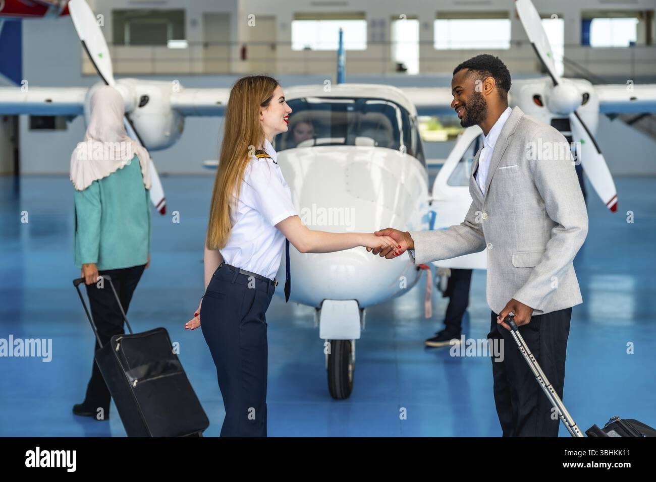Eine Pilotin schüttelt mit einem Geschäftsmann in einem Flugzeughangar die Hand und begrüßt einen Passagier vor einem Privatflug Stockfoto
