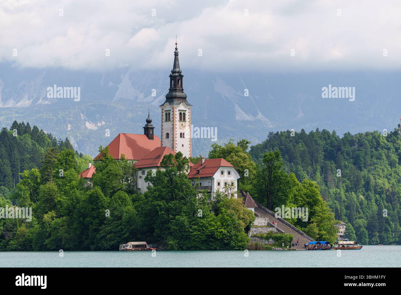 Ein traumhafter Blick auf den Bleder See in Slowenien mit blühenden Kastanienbäumen, die die Inselkirche vor den üppigen Hügeln der Alpen umrahmen. Hochwertige Fotos Stockfoto