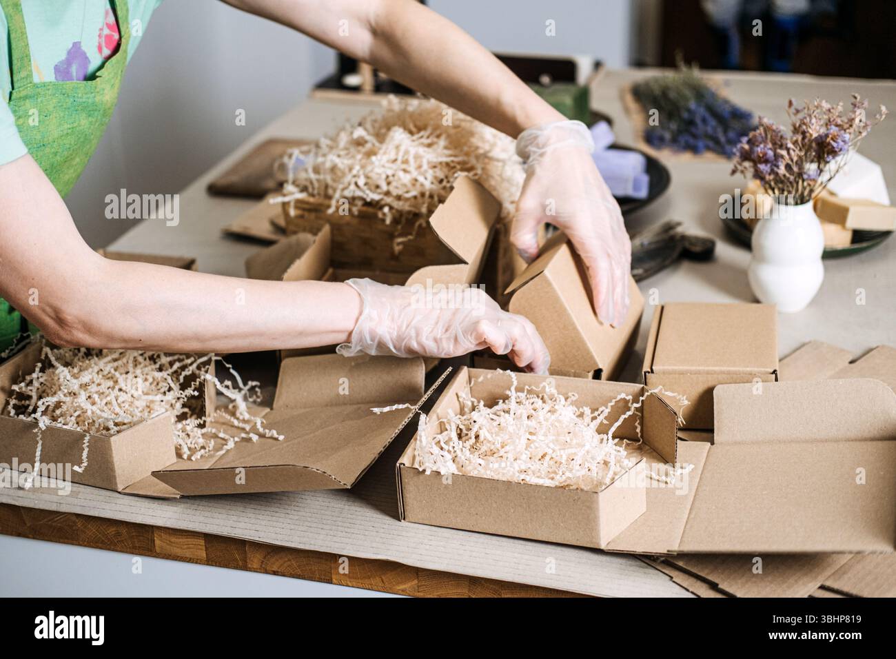Hände mit Handschuhen Verpacken Sie grüne Seifen und Lavendelseifen mit getrocknetem Lavendel in eine Geschenkbox aus Kraft. Achtsames Einkaufen, langsames Leben, ethische Produktion, bewusst Stockfoto