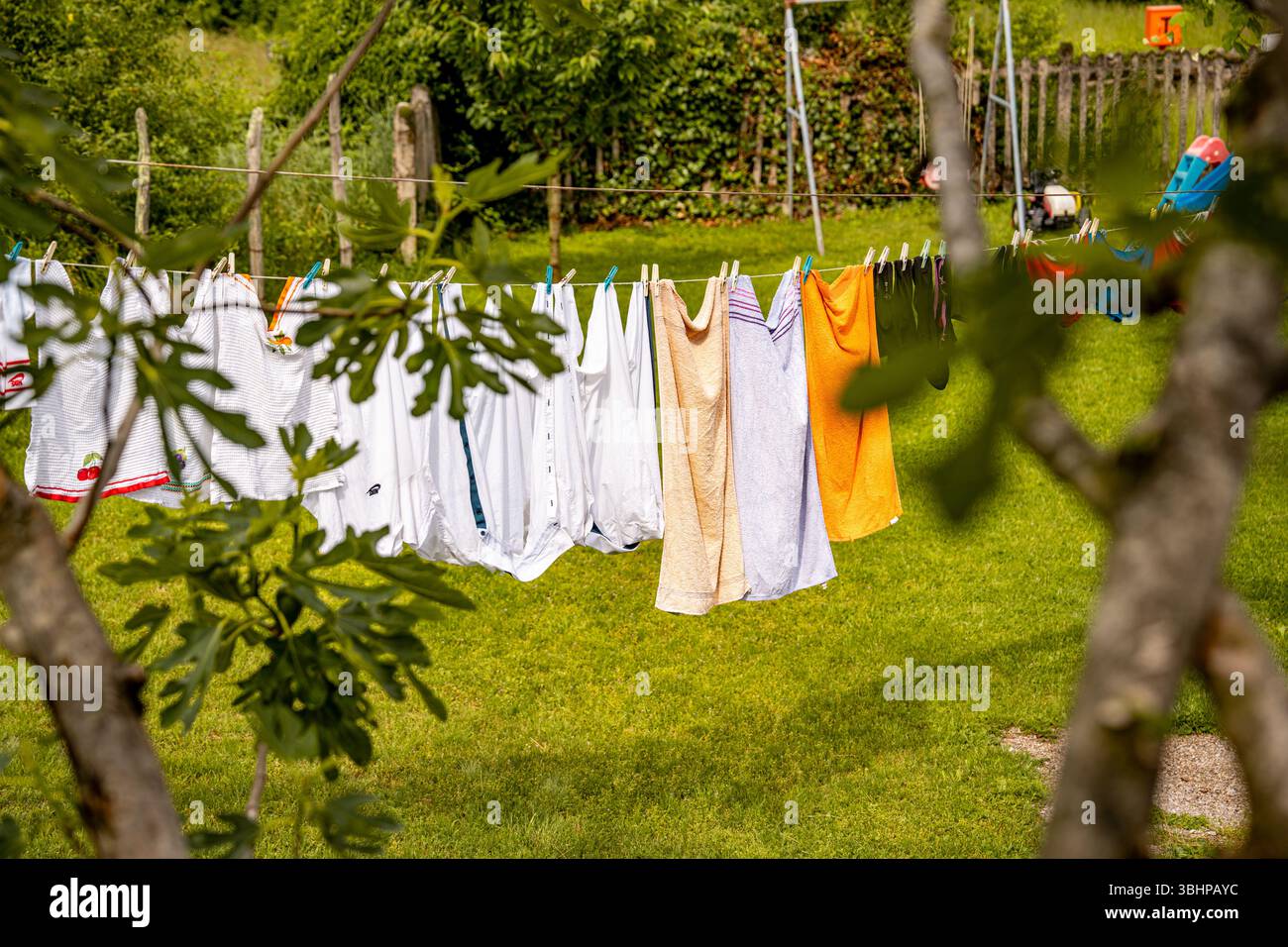 Bunte Wäschetrocknung auf der Kleidung im Sunny Garden: Frisch gewaschene Bettwäsche hängt zwischen Bäumen auf Einem grünen Rasen in Einer friedlichen Landschaft. Stockfoto
