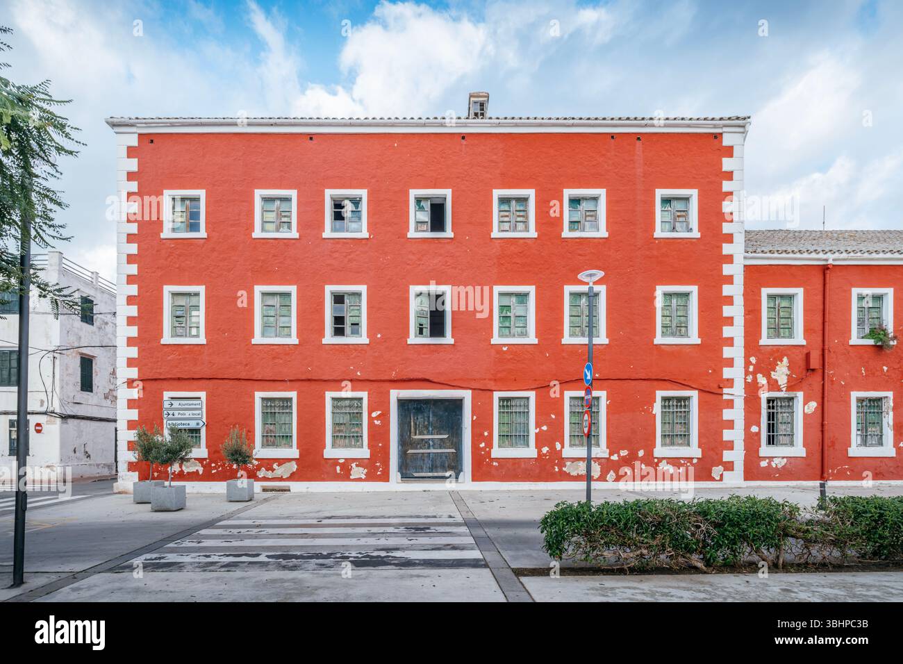 Markantes rotes Gebäude mit weißem Zierwerk und mehreren Fenstern in Einer menorquinischen Stadt. Mediterrane Architektur, Lebhafte Fassade, Spanisches Inselleben, Urban Stockfoto