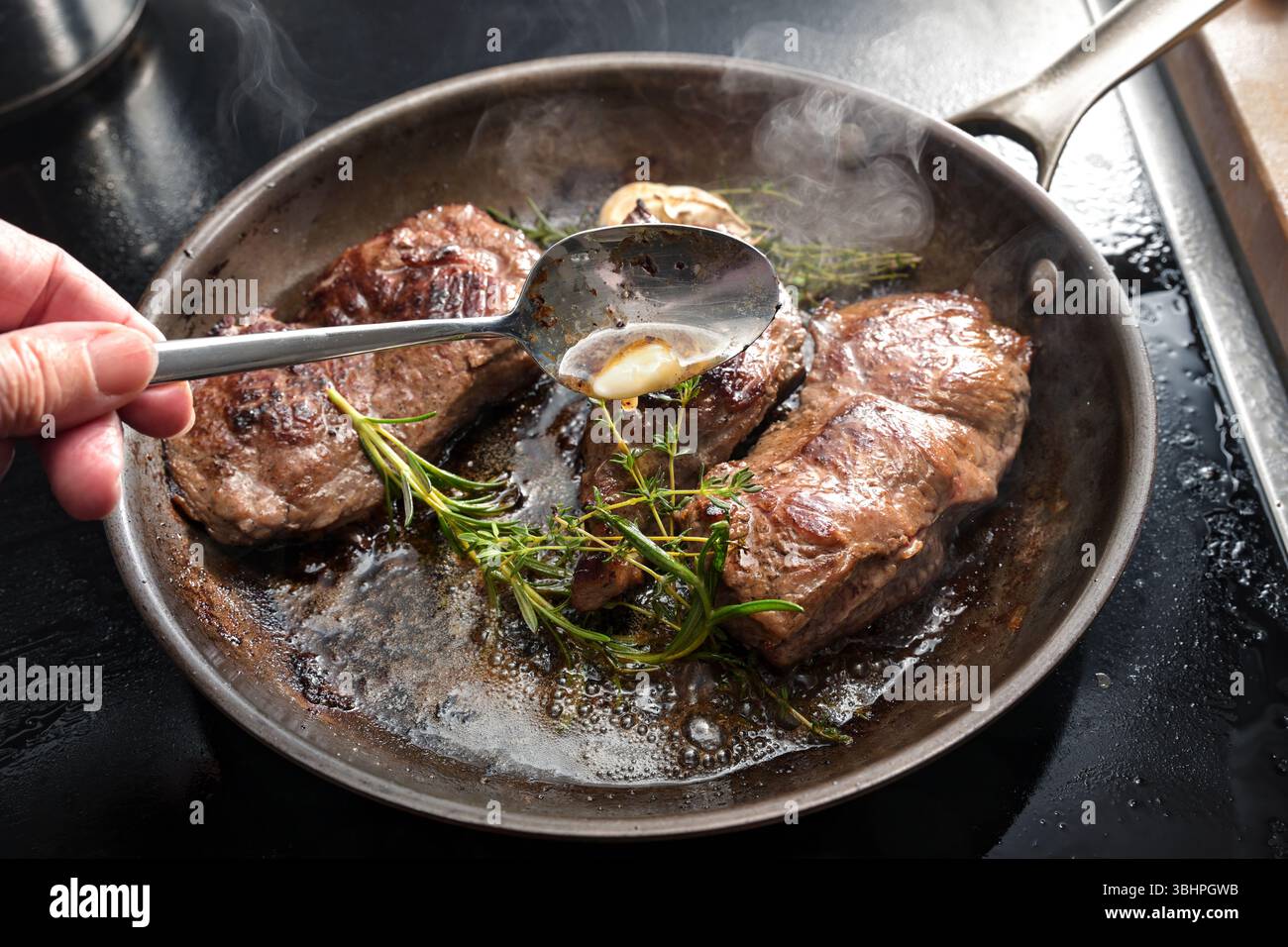 Frisch geröstete Rindersteaks werden mit Butter, Knoblauch, Thymian und Rosmarin in einer Karbonstahlpfanne serviert. Hausgemachte Gerichte mit leckerem Fleisch, Auswahl Stockfoto Frisch geröstete Rindersteaks werden mit Butter, Knoblauch, Thymian und Rosmarin in einer Karbonstahlpfanne serviert. Hausgemachte Gerichte mit leckerem Fleisch, Auswahl Stockfoto
