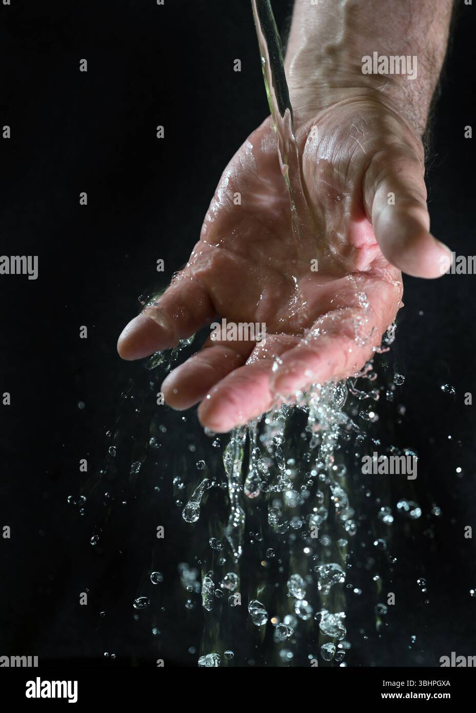 Wasser, das über die Hand eines Mannes fließt und glitzernde Tropfen vor schwarzem Hintergrund spritzt, Konzept für eine nachhaltige Lebensumwelt auf der Erde, Stockfoto