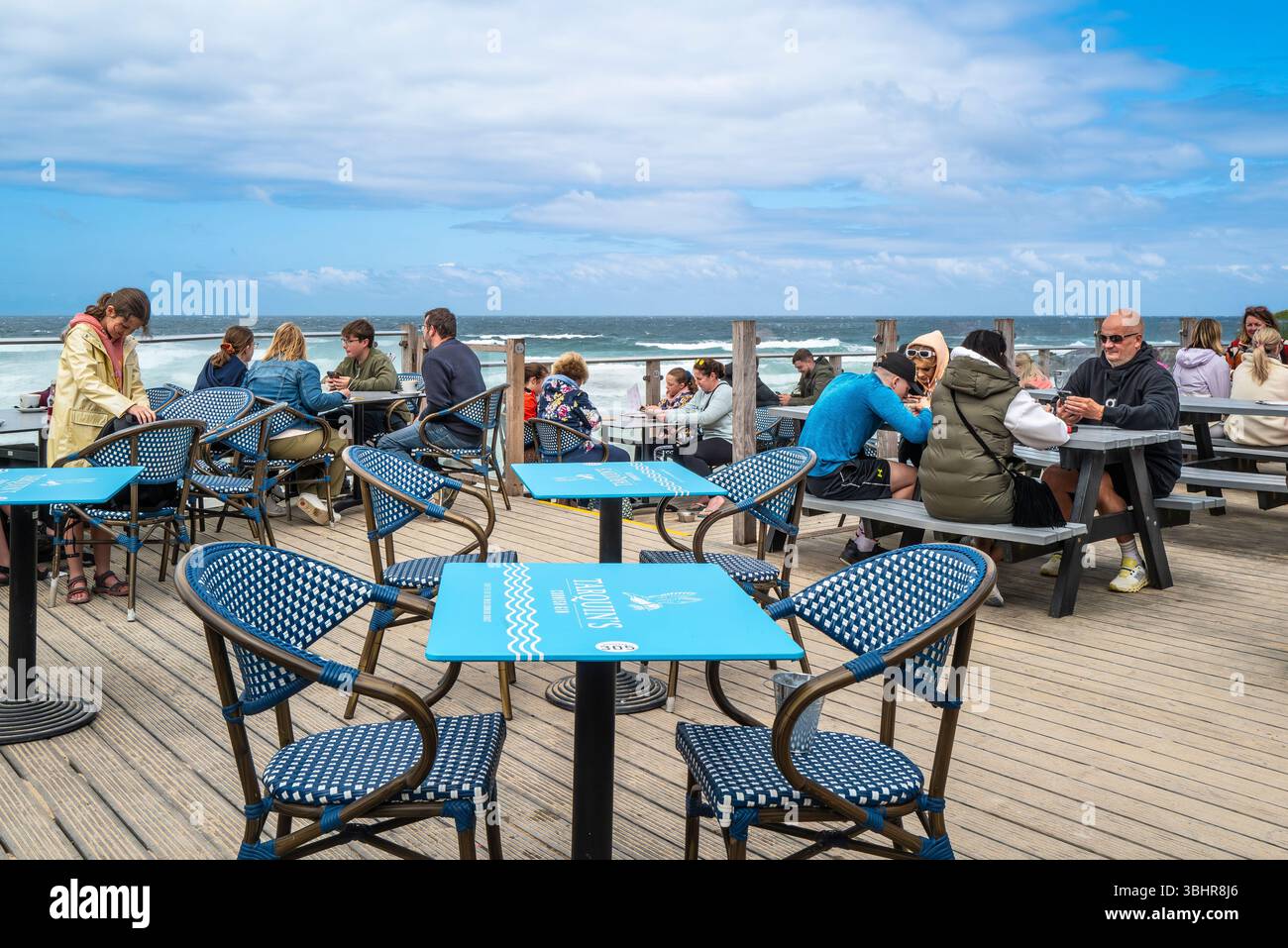 Urlauber sitzen an Picknicktischen auf dem Terrassenbereich der Fistral Beach Bar in Newquay in Cornwall, Großbritannien. Stockfoto