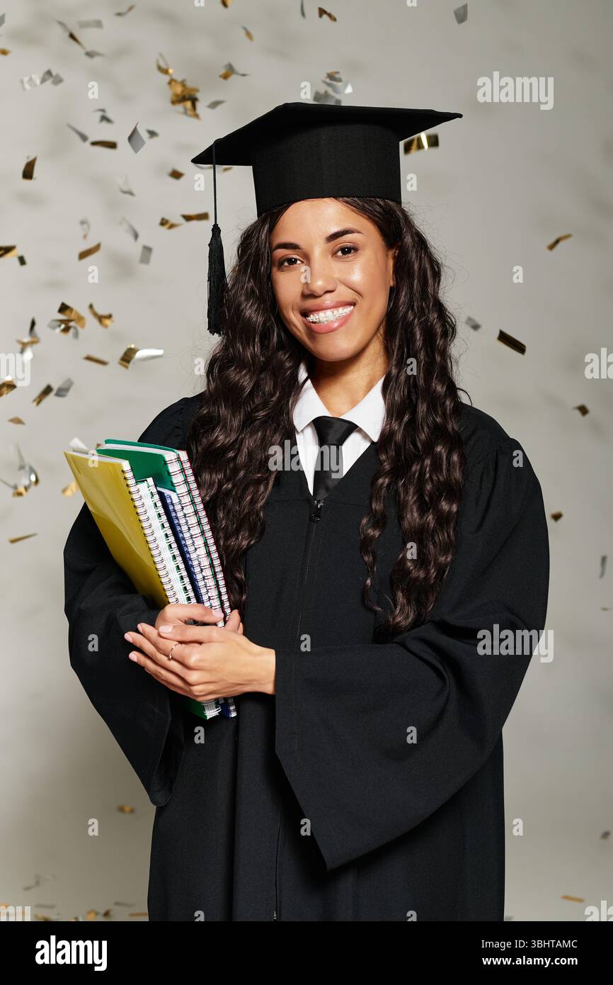 Eine junge Frau im Kleid lächelt mit Büchern, während Konfetti um sie herum fällt. Stockfoto