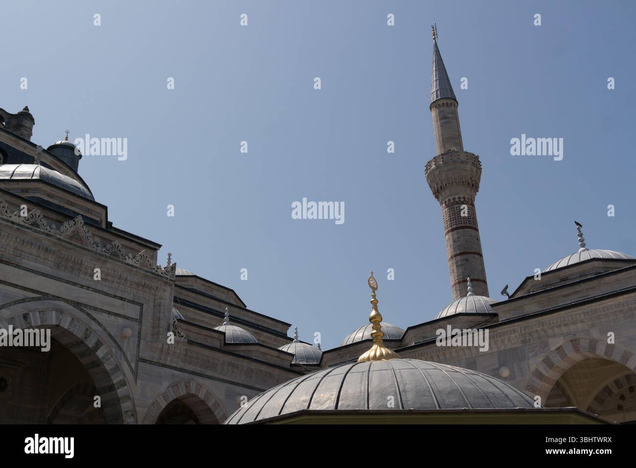 Besucher bewundern das komplizierte Design einer berühmten Moschee in Istanbul mit ihrem majestätischen Minarett und Kuppeldächern vor dem pulsierenden Himmel. Stockfoto
