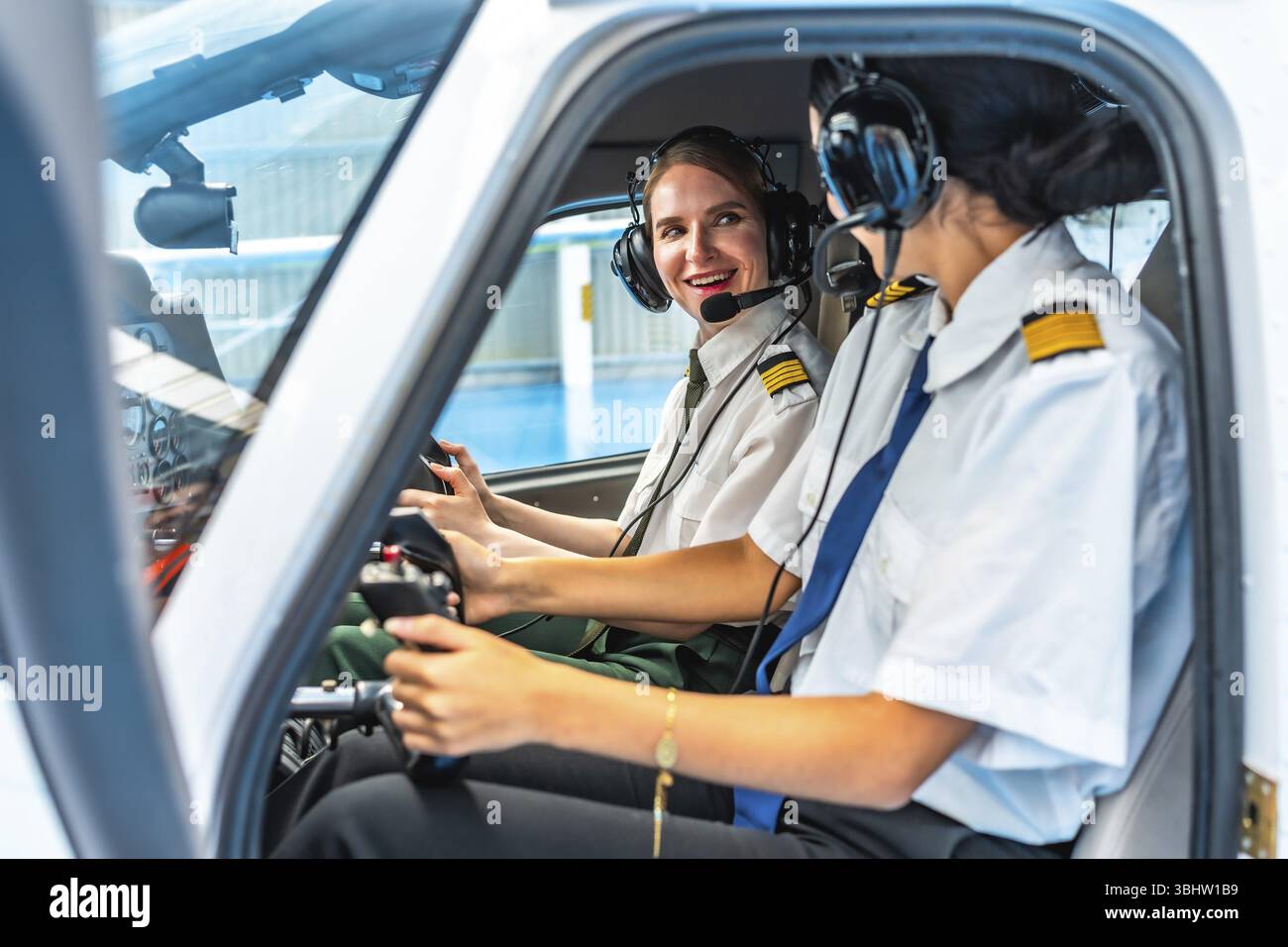 Zwei lächelnde Piloten in Kopfhörern und Uniformen sitzen im Cockpit eines kleinen Flugzeugs, bedienen die Steuerung und kommunizieren Stockfoto