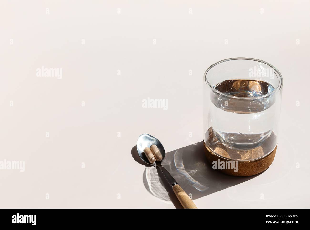 Zwei Pillen auf Löffel und Glas Wasser sind bereit für die tägliche Einnahme von Vitaminen, die Gesundheit und Wellness fördern. Stockfoto