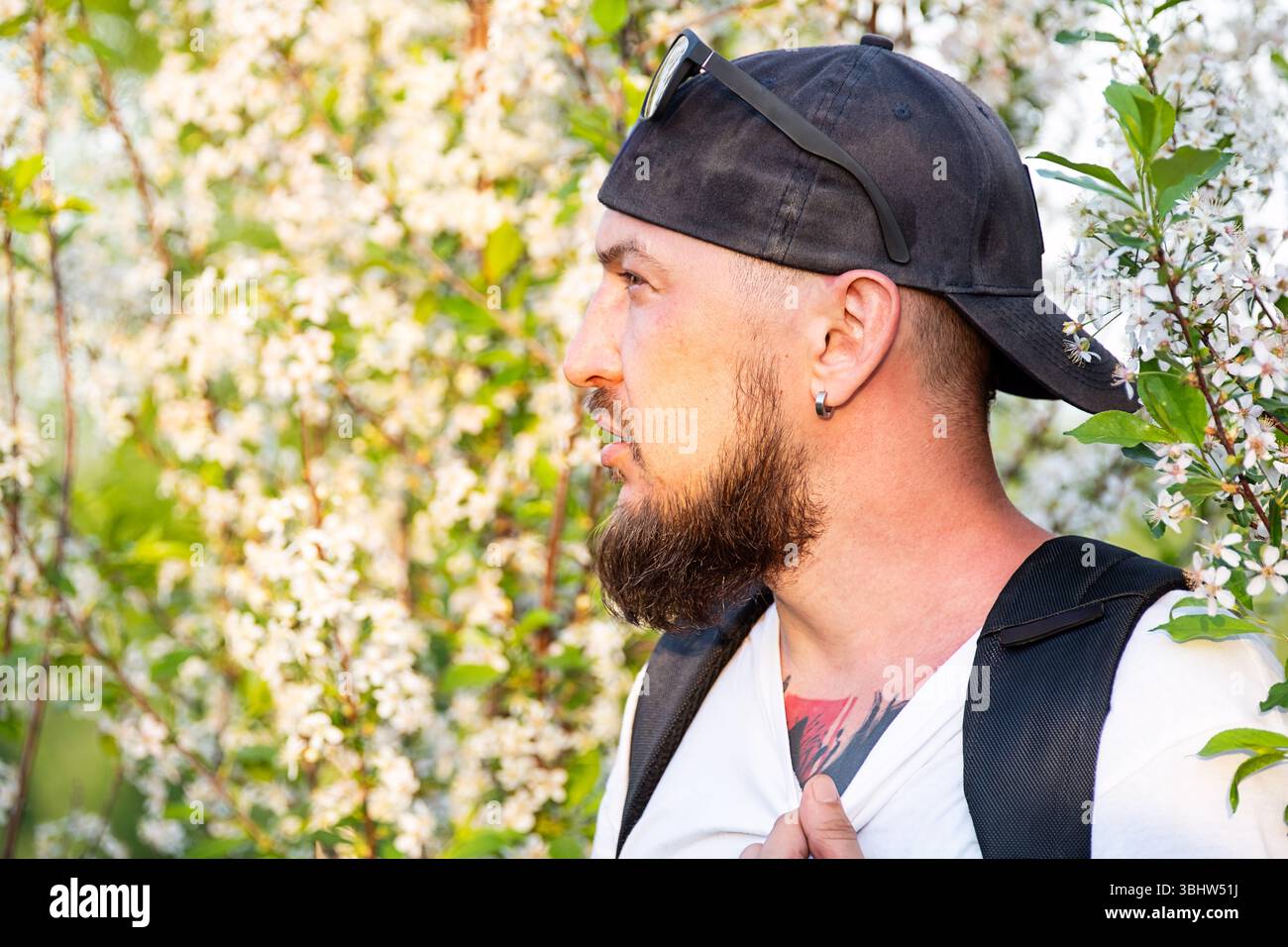 Porträt eines Mannes mit Bart in Baseballmütze gegen den weißen Blumenbaum im Frühling. Stockfoto