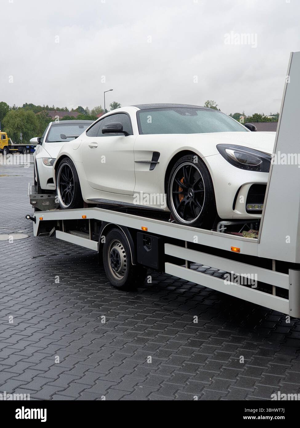 Zwei Sportwagen werden von einem LKW transportiert. Einzelwagen-Transporter mit Anhänger: Weißer Mercedes-AMG auf dem Transportwagen und weißer BMW auf dem Anhänger. Stockfoto