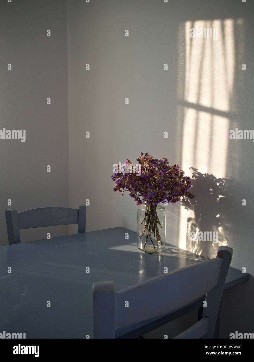 Minimalistischer blau-grauer Tisch mit Lavendelstrauß in warmem Licht. Stockfoto