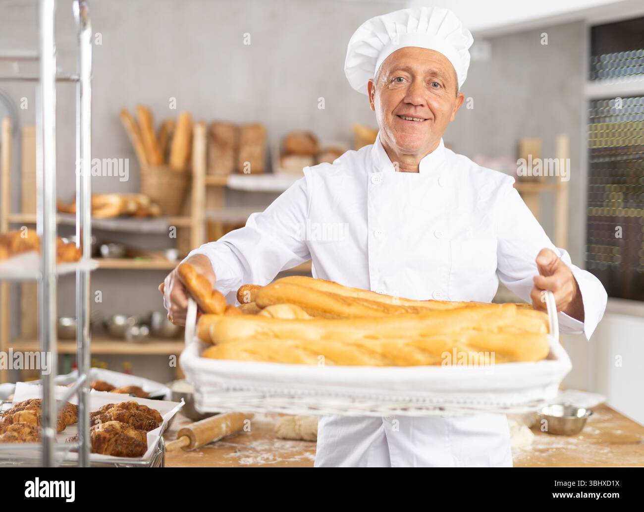 Lächelnder älterer Bäcker, der ein Tablett mit goldenen Baguettes hält Stockfoto