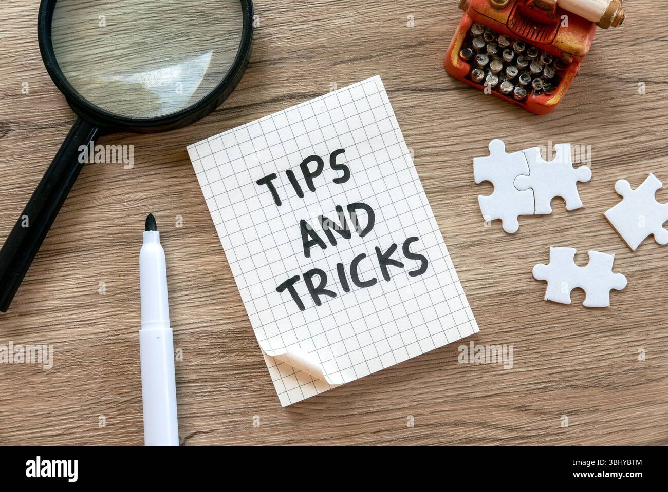 Tips and Tricks Notizbuch mit Vergrößerungsglas, Puzzleteilen und Miniatur-Schreibmaschine auf Holztisch Stockfoto