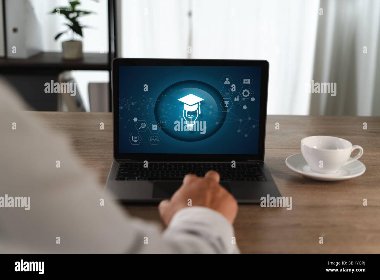 Eine Person auf E-Learning-Plattformen, die vor dem Laptop auf einem Holztisch sitzt und ein Symbol für digitale Bildung oder Lernen mit Graduierungskappe und Glühbirne darstellt Stockfoto