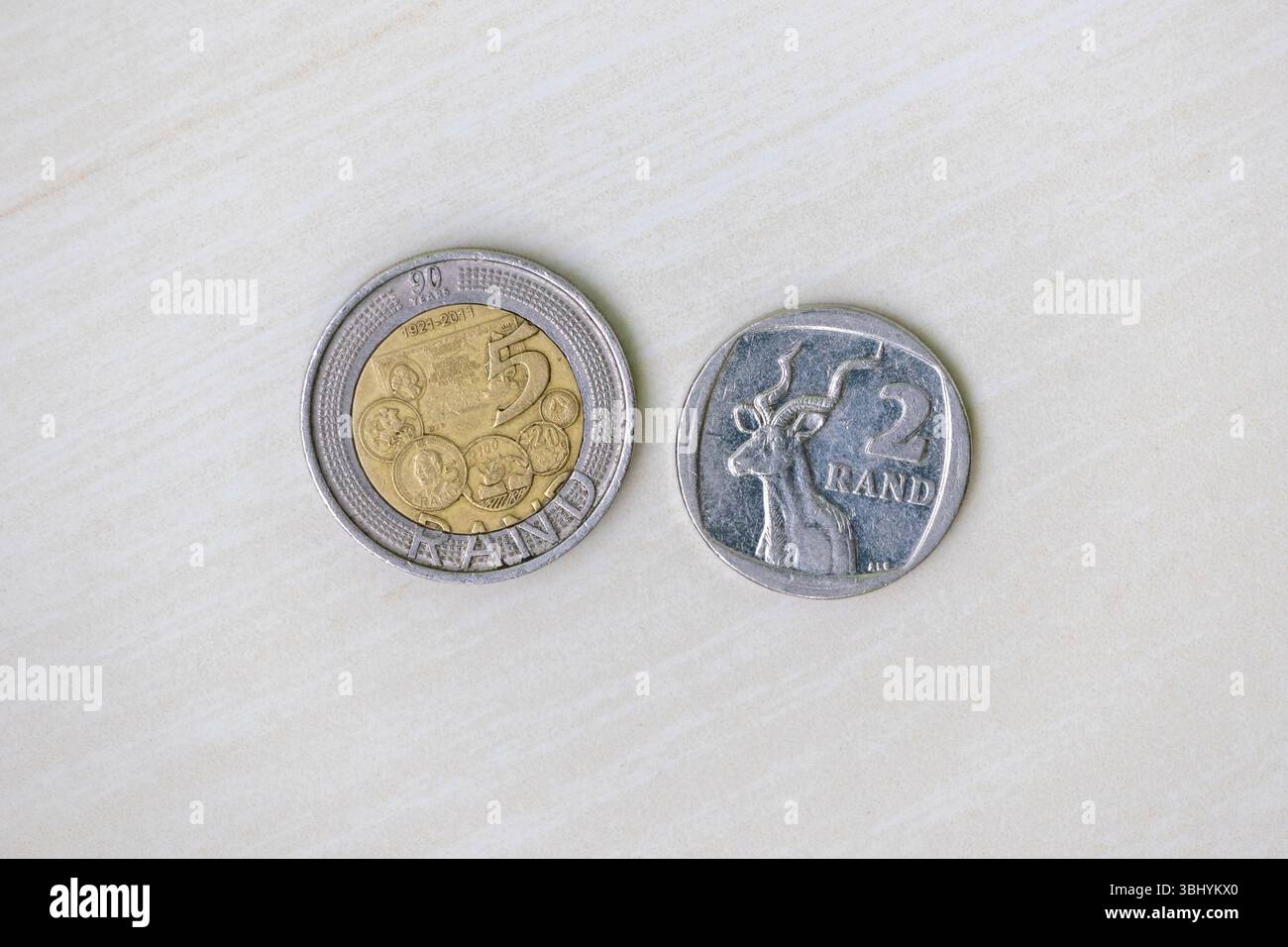 Zwei Rand- und fünf Rand-südafrikanische Münzen auf einer hellen Holzoberfläche. Draufsicht auf die südafrikanische Währung. Stockfoto