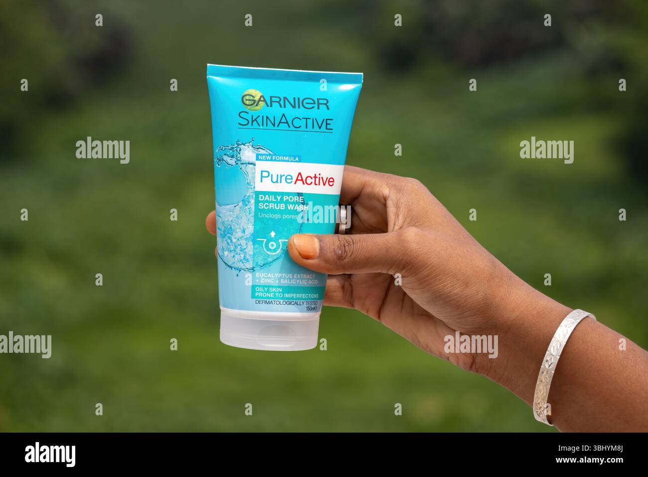 Weibliche Hand hält Garnier Skin Active Daily Pore Scrub Gesichtswaschrohr mit grünem Naturhintergrund. Gesichtsreiniger entfernt Schmutzöl. Stockfoto