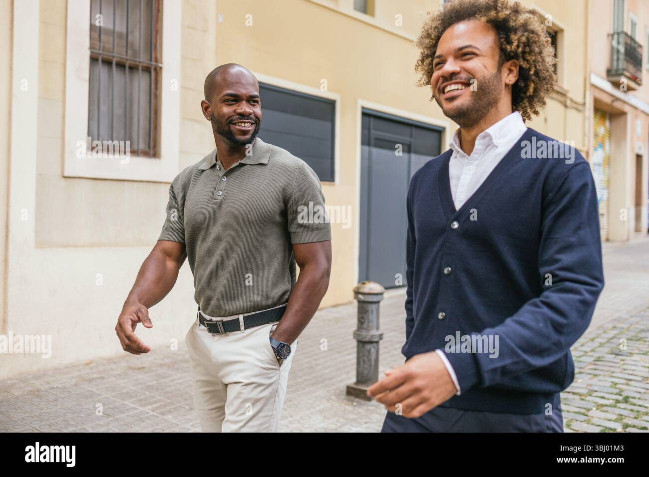 Zwei Kollegen, die in einer sonnigen Straße in Barcelona spazieren gehen und sich unterhalten, genießen ein zwangloses Meeting außerhalb des Büros. Sie wirken entspannt und engagiert Stockfoto