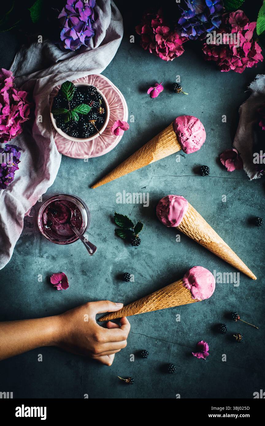 Verführerische Eiskegel mit cremigem griechischem Joghurt, reichhaltiger Sahne und wilder brombeermarmelade. Perfekt arrangiert mit frischen Brombeeren und leuchtenden Blumen Stockfoto