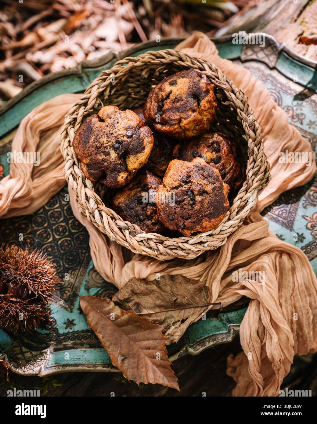 Ein rustikaler Korb gefüllt mit frisch gebackenen Kürbismuffins auf einer aufwendig gemusterten Oberfläche. Herbstdekor unterstreicht die gemütliche und gemütliche Atmosphäre Stockfoto