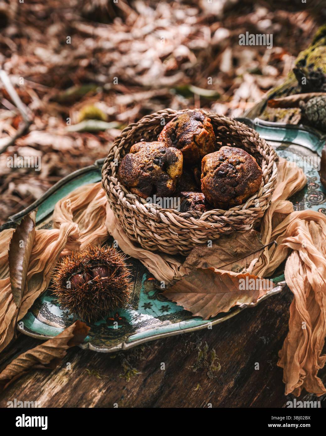Ein gewebter Korb mit frisch gebackenen Kürbismuffins liegt auf einem dekorativen Tablett. Die Herbststimmung mit Blättern und warmen Tönen rundet diese gemütliche Atmosphäre ab Stockfoto