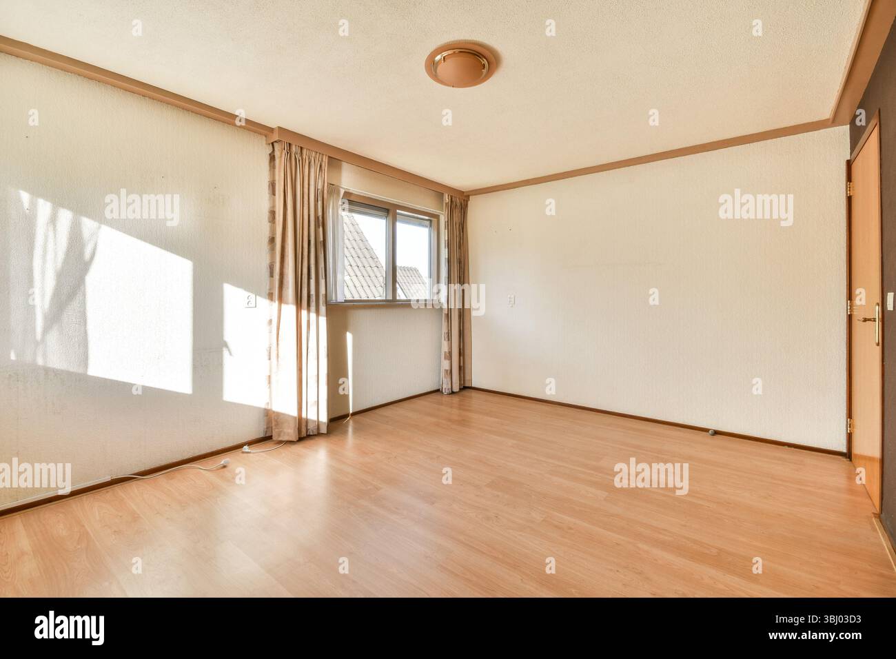 Ein geräumiger, heller und minimalistischer leerer Raum mit natürlichem Licht durch ein Fenster, Holzfußboden und einfacher Einrichtung. Stockfoto