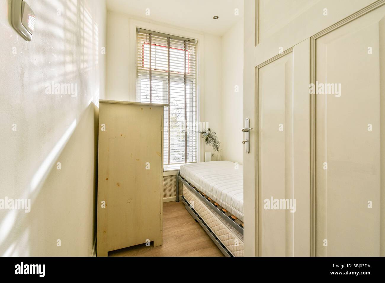 Ein heller und gemütlicher Raum mit einem Holzschrank und einem gepflegten Bett, ergänzt durch natürliches Licht durch das Fenster Stockfoto
