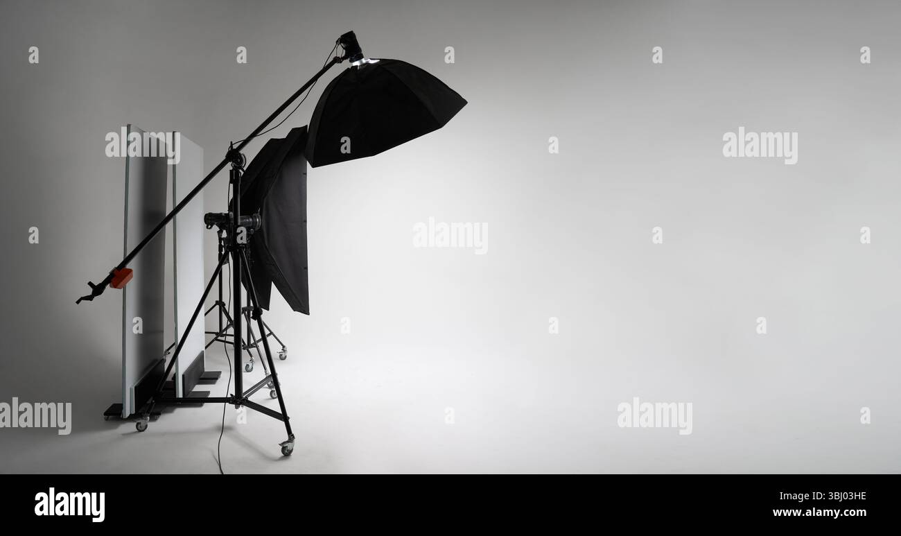 Ein professionelles Fotostudio mit einem robusten Stativ mit montierten Studio-Blitzlichtern und einer großen Softbox vor einem weißen Hintergrund Stockfoto