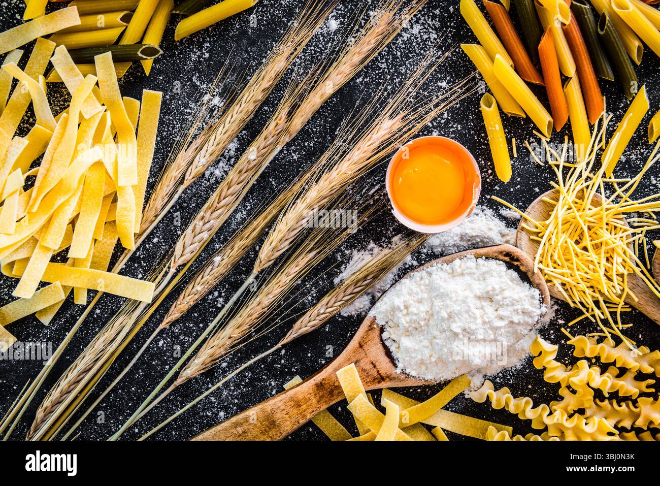 Rohe Teigwaren, Mehl und andere Produkte auf einem schwarzen, strukturierten Tisch Stockfoto