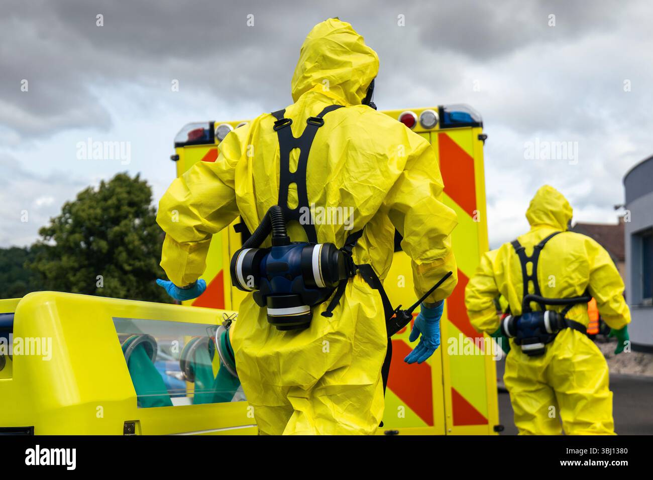 Mitglieder des Biohazard-Teams des Rettungsdienstes in Schutzanzug gegen Krankenwagen während der Ausbildung. Stockfoto