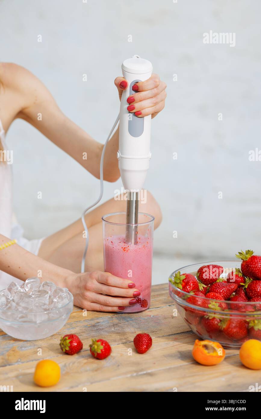 Frischer Erdbeeren-Smoothie mit Stabmixer auf rustikalem Tisch mixen. Natürliche Zutaten, gesunder Lebensstil, Sommererfrischung. Stockfoto