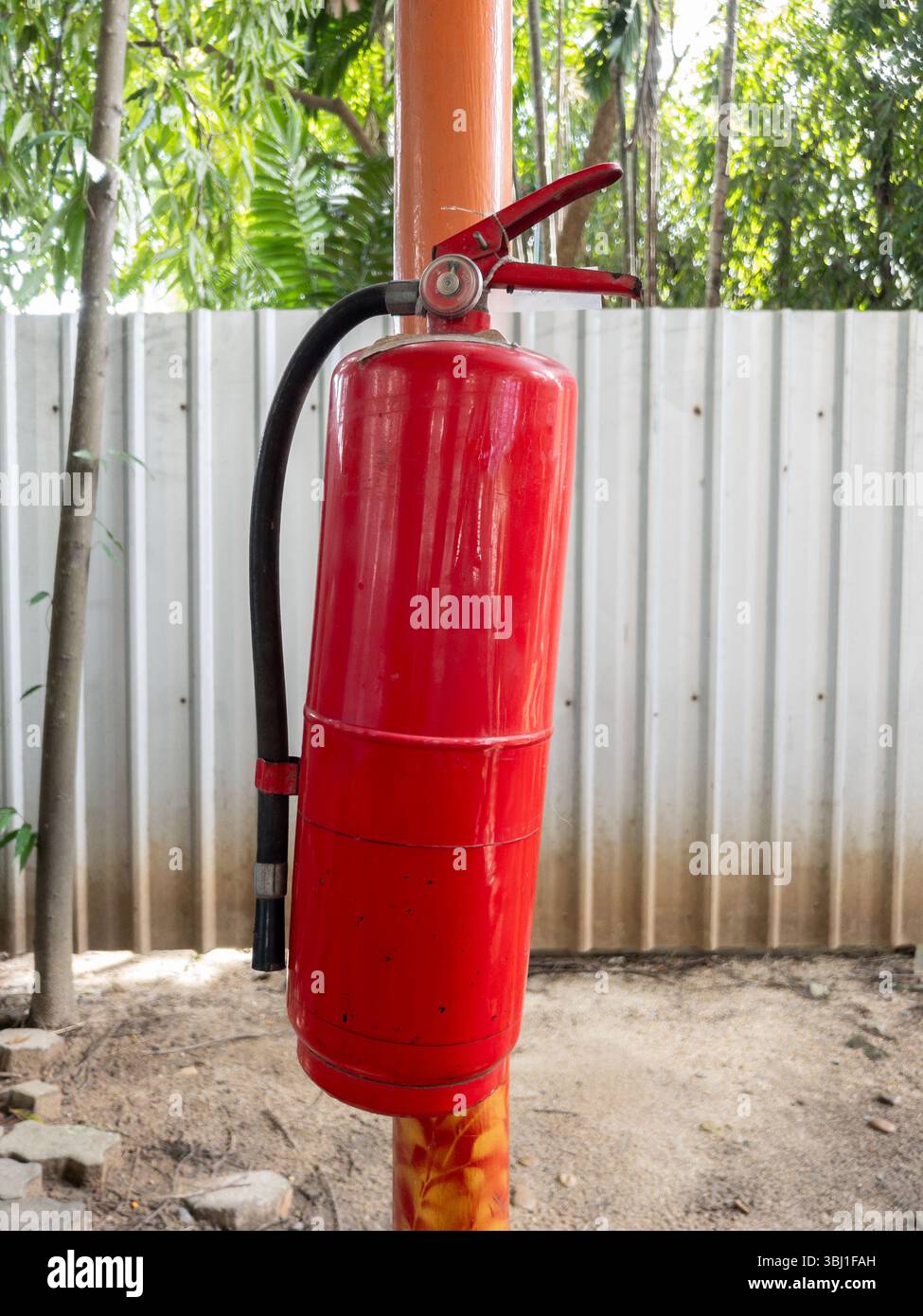 Auf einer Baustelle ist ein roter Feuerlöscher mit Bäumen und einem Zaun montiert. Wichtige Sicherheitsausrüstung für Brandfälle Stockfoto