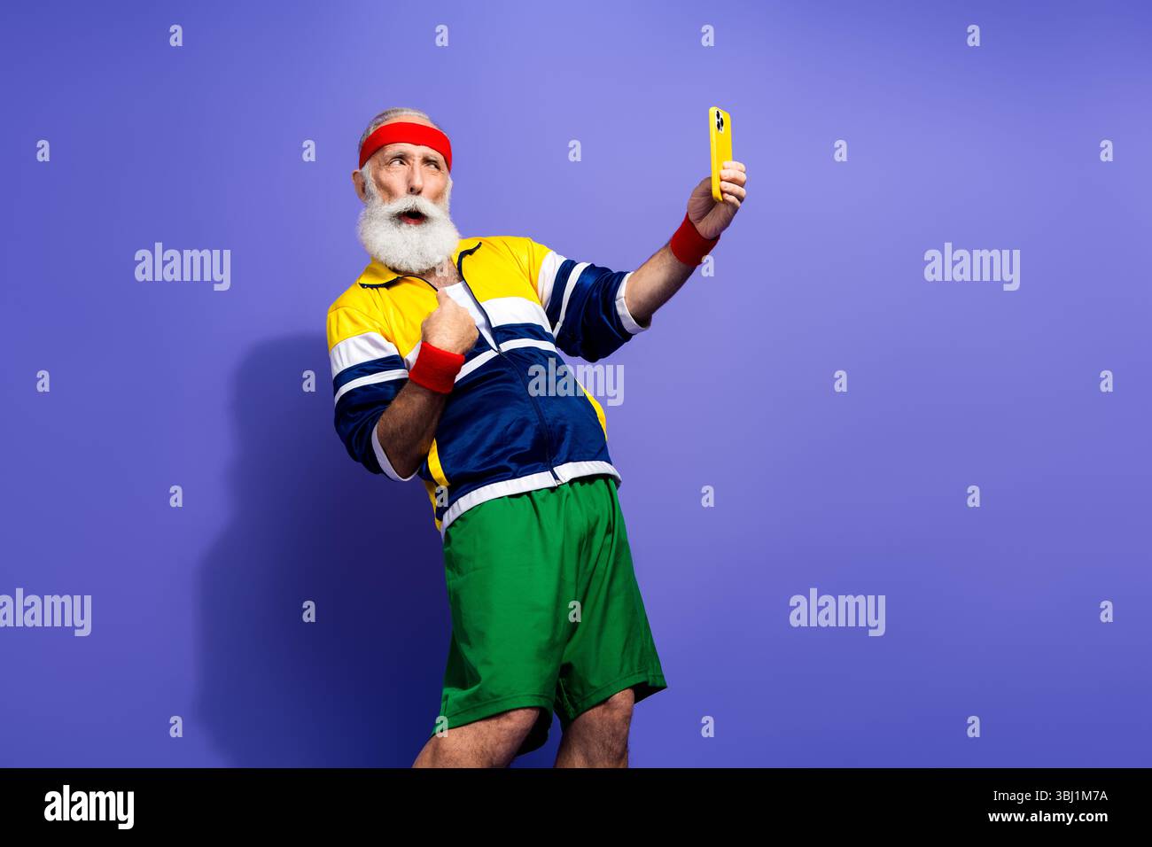 Funky Mann in Retro-Sportbekleidung, der mit einem Telefon posiert und eine lebendige Persönlichkeit und klassische Ästhetik der 80er Jahre in lebendiger, farbenfroher Umgebung demonstriert Stockfoto