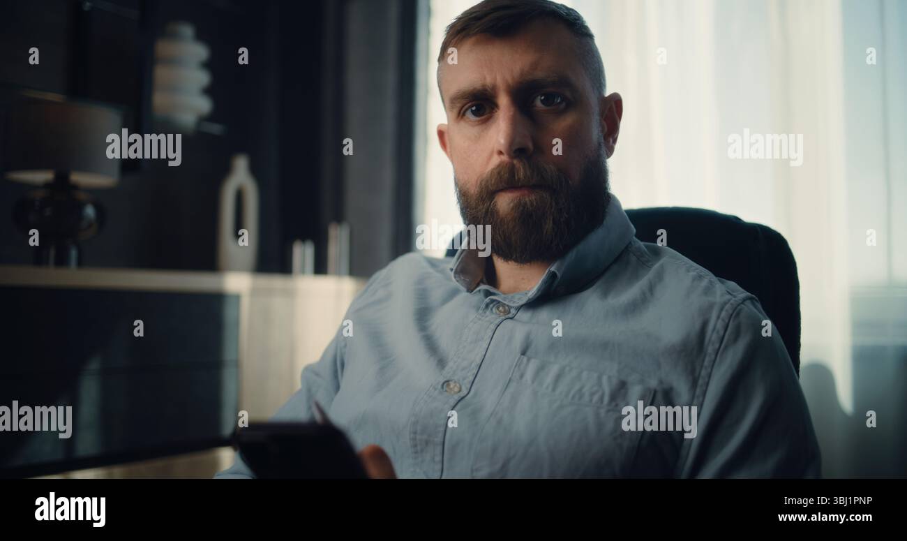 Professioneller Finanzexperte arbeitet am Smartphone, überwacht Echtzeitaktien, Börsenkarten, Blick auf die Kamera. Porträt des erfolgreichen Geschäftsmannes im komfortablen Büro der Investitionsbank Stockfoto