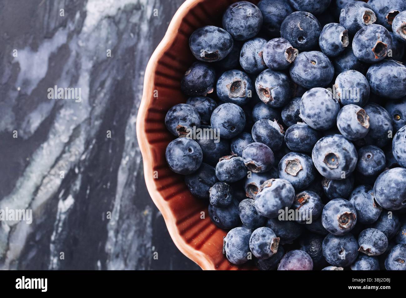 Frische Heidelbeeren in roter Schüssel. Saftige Bio-Früchte auf schwarzem Marmor. Sommer Antioxidans Superfood. Leckere süße Beeren. Gesunde Dessert Nahaufnahme. Stockfoto