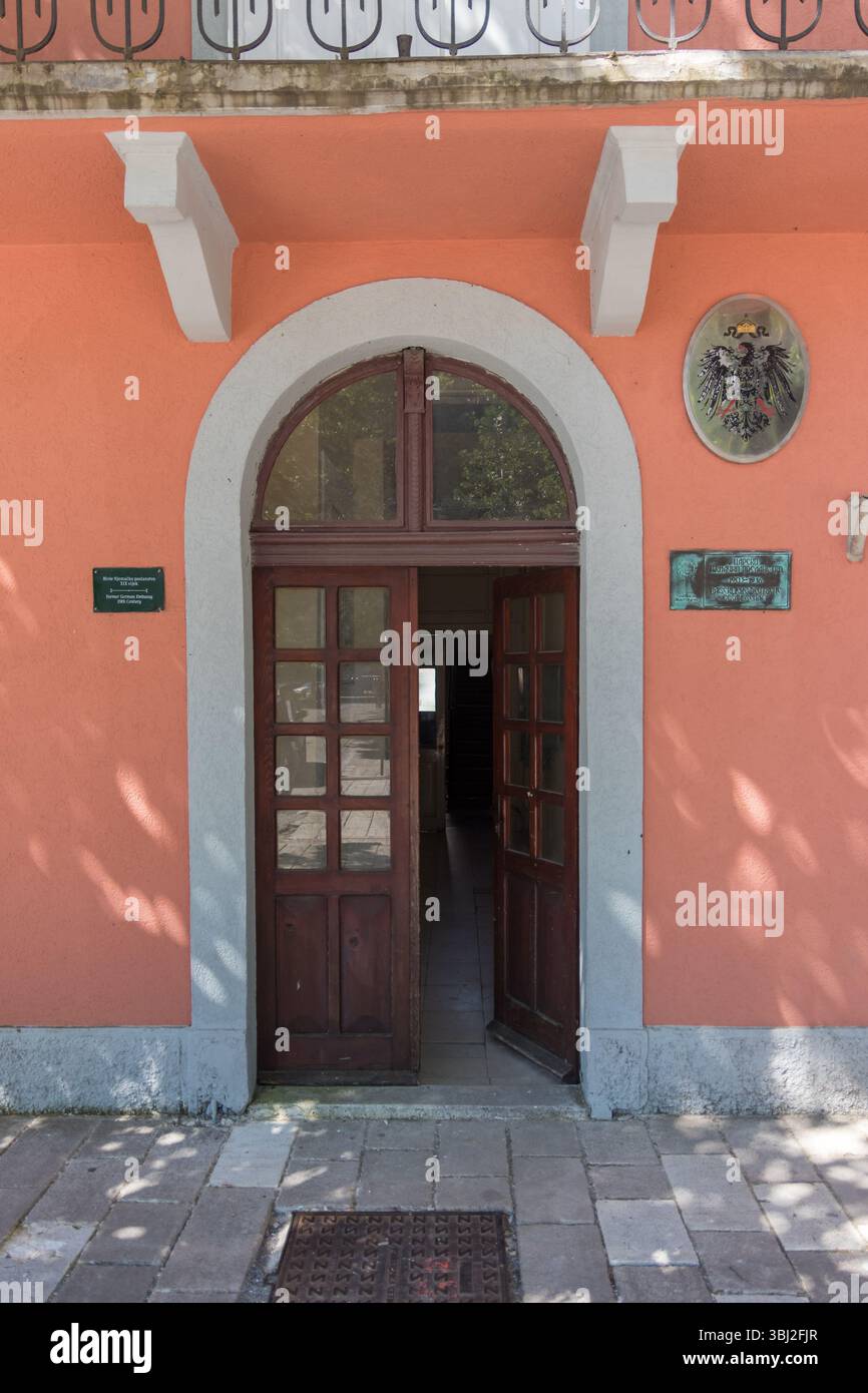 CETINJE, MONTENEGRO, 06.25.2019: Illustration einer bogenförmigen Holztür auf einem pfirsichfarbenen Gebäude, in dem traditionelle architektonische Details beleuchtet werden Stockfoto