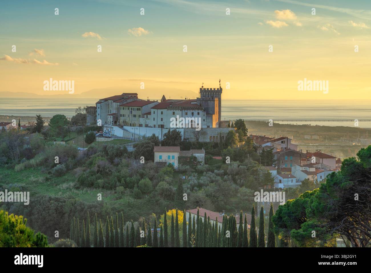Blick von oben auf die Stadt Rosignano Marittimo und die Burg. Meer im Hintergrund bei Sonnenuntergang. Toskana, Italien Stockfoto