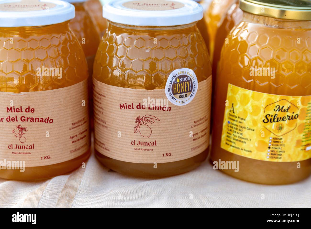 Denia, Alicante - Spanien - 12-01-2024: Glasgläser gefüllt mit goldenem Honig, mit strukturierten Wabenmustern und handwerklichen Etiketten, ausgestellt in A Stockfoto