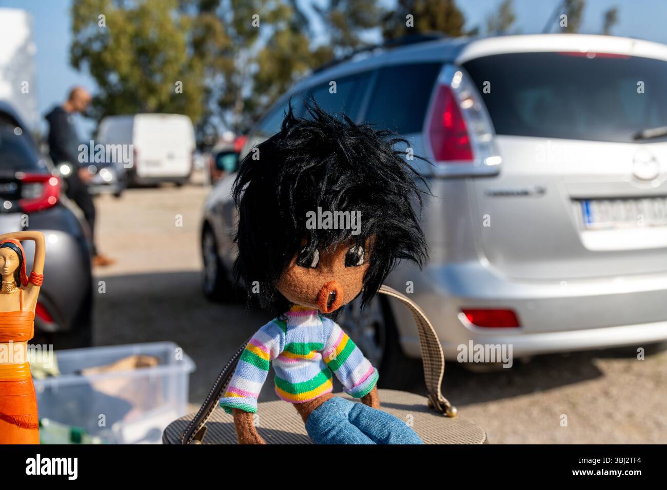 Denia, Alicante - Spanien - 12-01-2024: Eine handgefertigte Stoffpuppe mit schwarzem zotteligem Haar, einem bunten gestreiften Pullover und einer Jeanshose, die auf einer Marke ausgestellt ist Stockfoto