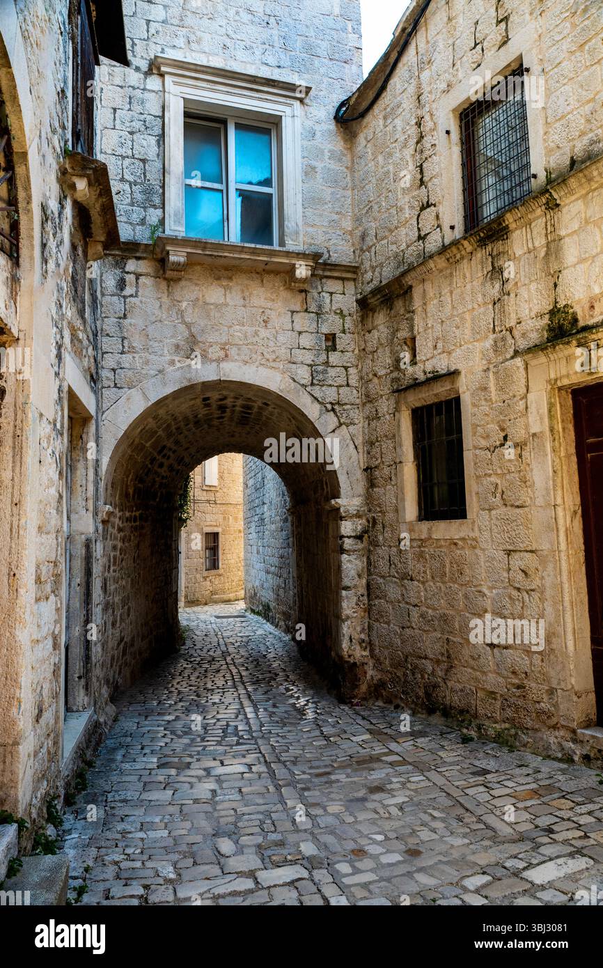 Dalmatische Architektur im romanischen Stil mit Tonnenbögen und Kopfsteinpflasterstraßen in Trogir, Kroatien. Stockfoto