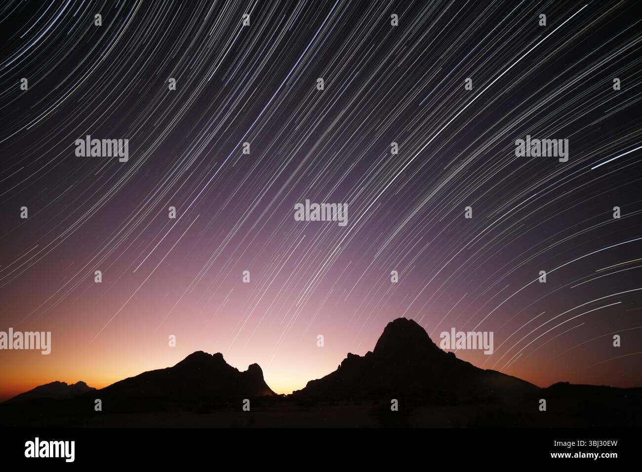 In der Abenddämmerung fängt eine lange Belichtung die nächtlichen Sterne ein, die über der Spitzkoppe in Usakos, Namibia, nachziehen. Stockfoto