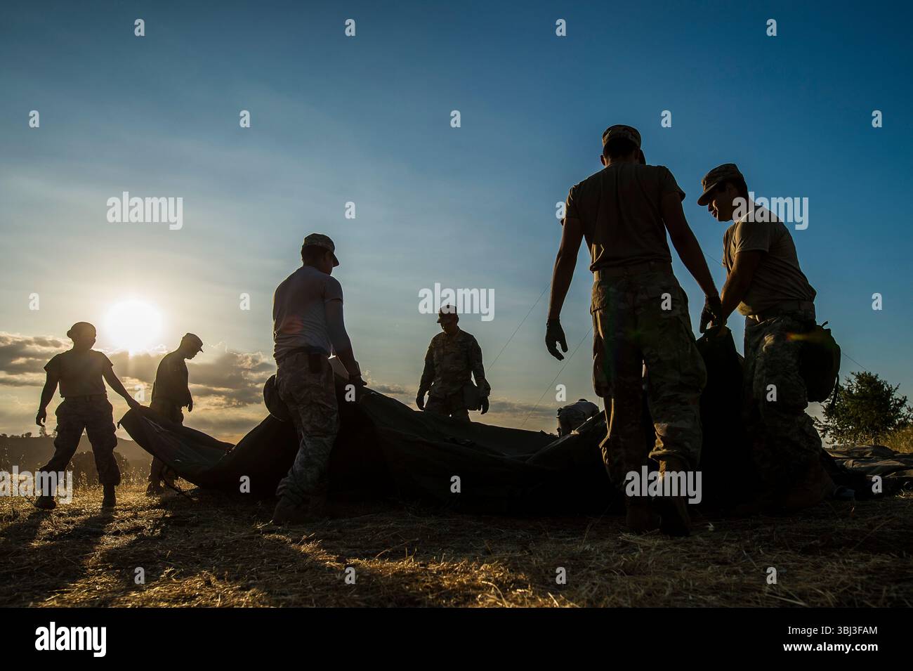 Soldaten der US-Armee arbeiten bei Sonnenaufgang zusammen, um ein Feldzelt in einem staubigen kalifornischen Trainingsbereich zu bauen, um Teamarbeit und Einsatzbereitschaft hervorzuheben. Stockfoto