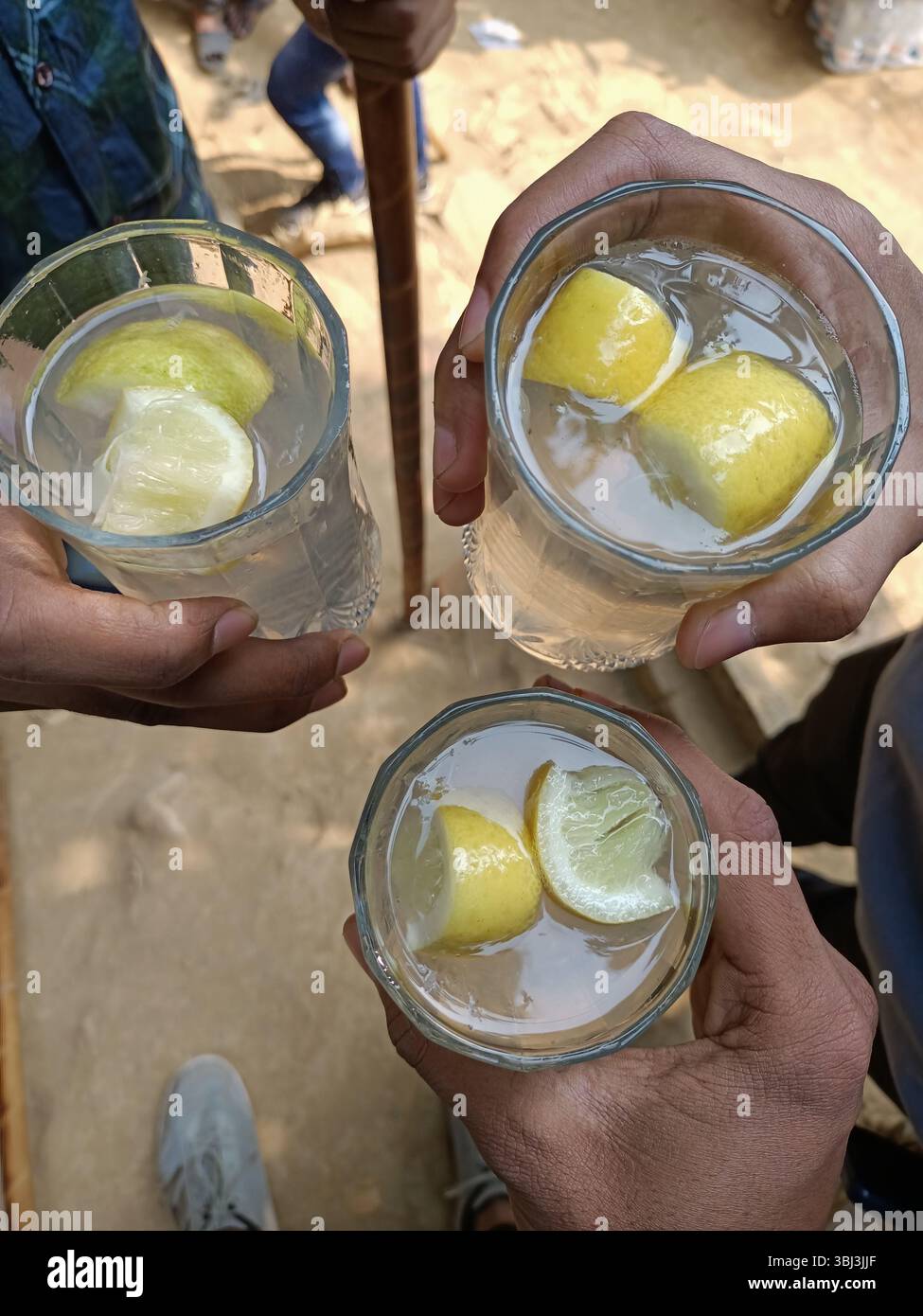 Ein erfrischendes Glas Zitronenwasser mit Freunden unter der warmen Sonne. Reine und lokale Hydration. - Smartphone-aufgenommenes Stockfoto