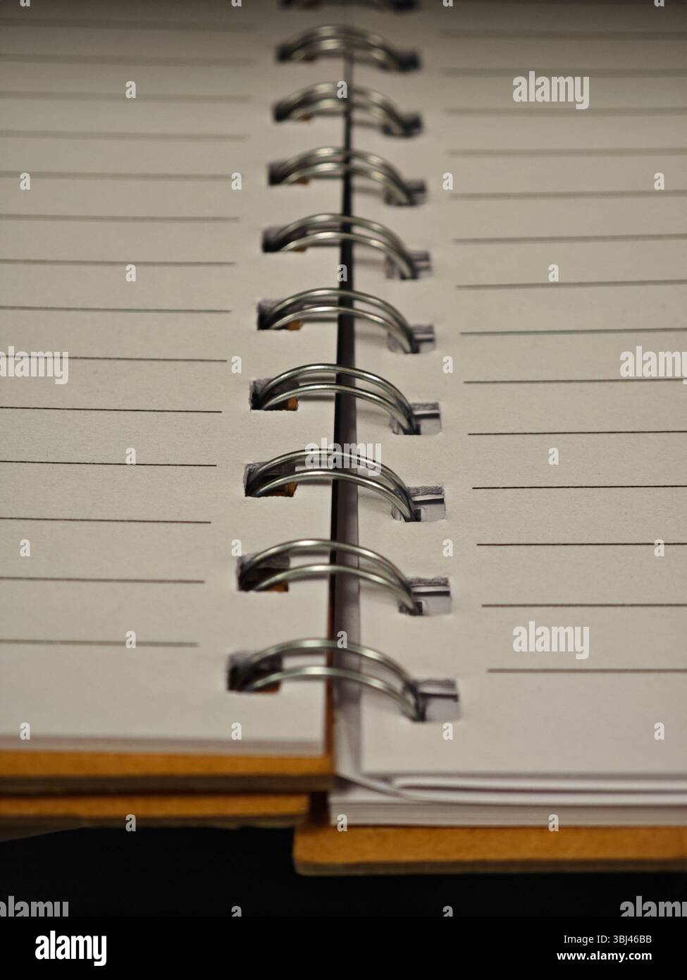 Ein leeres Notizbuch liegt offen auf einem Holztisch, dessen Spiralbindung sichtbar ist. Die leeren Seiten laden zum Schreiben oder Zeichnen ein, perfekt zum Schreiben von Gedanken Stockfoto