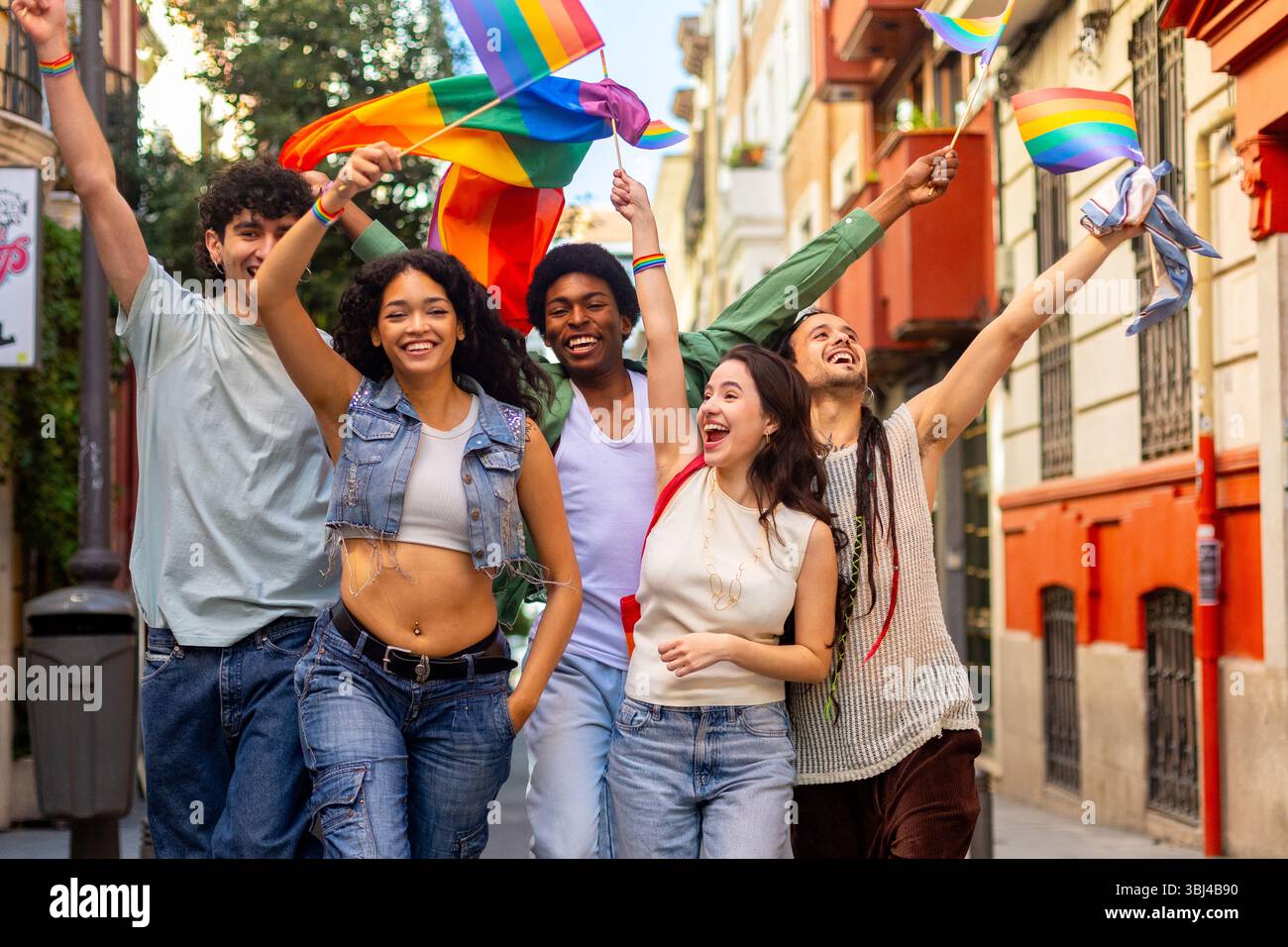 Eine Gruppe fröhlicher, multirassischer Menschen, die die Straße hinunterlaufen und Regenbogenfahnen schwenken, um den Stolz der Schwulen zu feiern Stockfoto