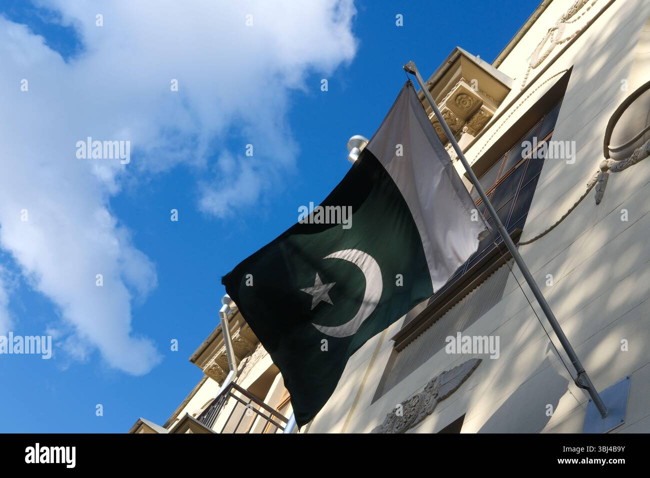 Pakistanische Flagge, die im Wind gegen blauen Himmel und historische Gebäude schwingt. Flagge von Pakistan. Flaggenfeier, Patriotismus. Botschaften und Konsulate Stockfoto