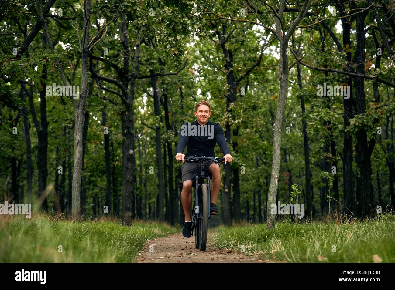 Ein fröhlicher und fröhlicher Mann fährt energisch mit seinem Mountainbike auf einem wunderschönen malerischen Weg, der sich durch einen lebendigen grünen Wald schlängelt, ganz ich Stockfoto